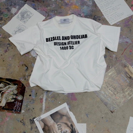 White t-shirt with text on a textured surface with scattered papers and images.